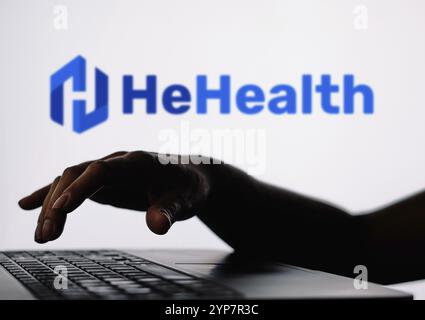 In dieser Abbildung ist das HeHealth-Logo im Hintergrund einer Silhouette einer Person zu sehen, die ein Notizbuch verwendet Stockfoto