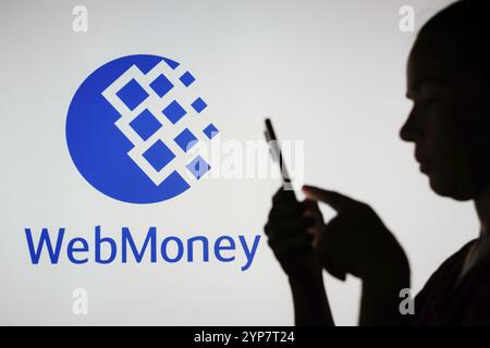 In dieser Fotoabbildung hält die Silhouette einer Frau ein Smartphone mit dem WebMoney-Logo im Hintergrund Stockfoto