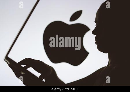In dieser Abbildung ist das Apple-Logo im Hintergrund einer Silhouette einer Person zu sehen, die ein Notebook verwendet Stockfoto