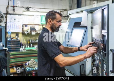 Reifer Mann, der am Bedienfeld einer Drehmaschine in einer cnc-Fabrik arbeitet Stockfoto