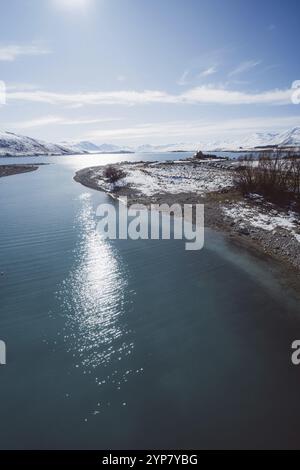 Sonnenspiegelung auf dem See mit schneebedeckten Bergen im Hintergrund unter blauem Himmel, Lake Tekapo, Neuseeland, Ozeanien Stockfoto