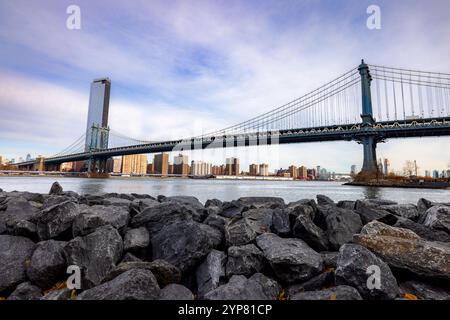 Die Manhattan Bridge erstreckt sich über den East River und verbindet Manhattan mit Brooklyn, eingerahmt von einem Vorboden aus zerklüfteten Felsen entlang der Küste. A Stockfoto