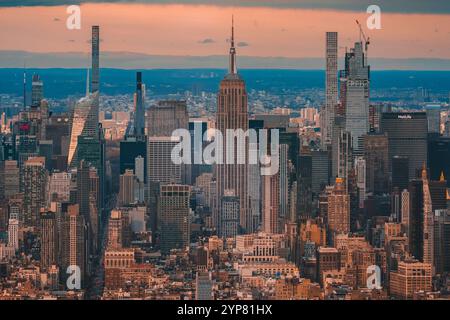 Ein atemberaubender Blick auf das ikonische Empire State Building, umgeben von den majestätischen Wolkenkratzern von Manhattan, die während des warmen Sonnenuntergangs gefangen wurden. Stockfoto