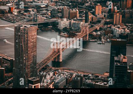 Aus der Vogelperspektive der berühmten Brooklyn Bridge, die den East River überspannt, mit der Skyline von Manhattan im Hintergrund, aufgenommen bei einem warmen und dramatischen Su Stockfoto