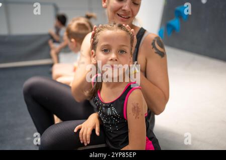 Niedliches Mädchen, das mit Mutter auf dem Boden im Boulderstudio sitzt. Lächelnde sportliche Athleten entspannen sich nach dem Training. Stockfoto