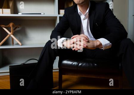 Geschäftsmann sitzt auf einem Stuhl vor dem Bücherregal Stockfoto