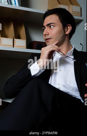 Geschäftsmann sitzt auf einem Stuhl vor dem Bücherregal Stockfoto
