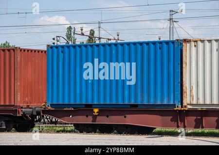 Ein blauer Frachtcontainer, der in einen Zug geladen wird und den intermodalen Verkehr und die Logistikbranche veranschaulicht. Stockfoto