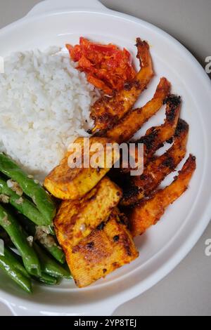 Hausgemachte indonesische Speisen, weißer Reis mit gegrillten Garnelen, sautierten grünen Bohnen, gegrilltem Tofu und Sambal. Stockfoto