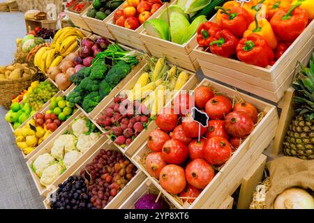 Frisches, farbenfrohes Obst und Gemüse sind ordentlich in Holzkisten am geschäftigen Marktstand angeordnet und ziehen Käufer an. Stockfoto