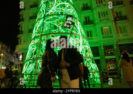 Madrid, Spanien. November 2024. Ein paar Küsse, während sie ein Selfie unter einem riesigen Weihnachtsbaum mit Lichtern machen, im Zentrum von Madrid, während die Weihnachtsbeleuchtung vom Madrider Stadtrat eingeschaltet wird. (Foto: Luis Soto/SOPA Images/SIPA USA) Credit: SIPA USA/Alamy Live News Stockfoto