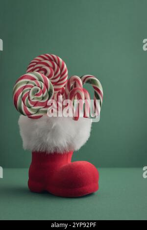 Weihnachtsbonbons und Lutscher im Weihnachtsmann-Stiefel auf grünem Hintergrund Stockfoto