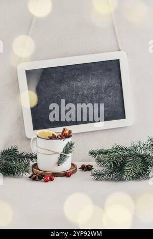 Becher mit heißem Getränk, Glühwein mit Orangenscheibe, Preiselbeere und Zimtstangen und gerahmte Tafel auf Hintergrund Stockfoto
