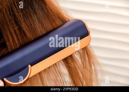 Nahaufnahme eines Haarglätters, der durch langes, hellbraunes Haar gleitet. Kosmetikmode und Styling-Werkzeuge Stockfoto