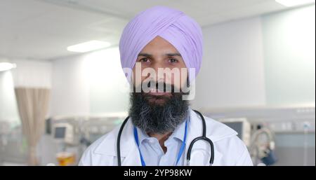 Porträt eines glücklichen birassischen sikh männlichen Arztes im Turban, der im Krankenhaus in Zeitlupe in die Kamera schaut Stockfoto