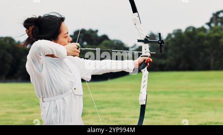 Feld, Bogenschütze und Frau mit Bogen, Ziel und Vorbereitung auf Wettkämpfe, Ausrüstung und Outdoor-Spiele. Wettkampf, Bogenschießen und Training vom Turnier Stockfoto