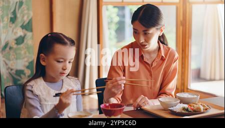 Mama, Mädchen und Essstäbchen beim Mittagessen, zu Hause oder beim Lehren für Essen, Essen oder Binden für Liebe im Esszimmer. Leute, Mutter und Tochter Familienhaus für Stockfoto