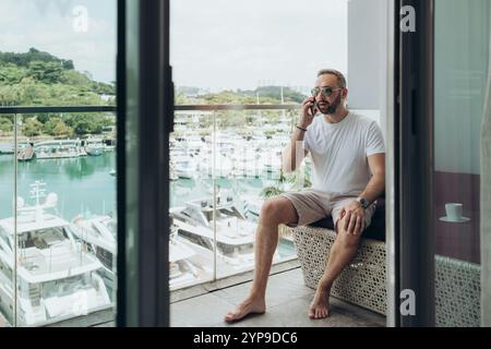 Mann in einem weißen T-Shirt, der auf dem Balkon telefoniert Stockfoto