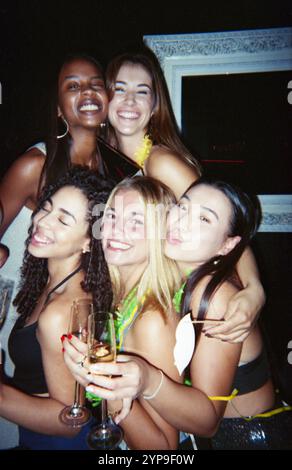 Eine Gruppe von Freunden feiert fröhlich mit Champagner in einer lebhaften Atmosphäre. Das Bild hat einen Vintage-Film-Look. Stockfoto