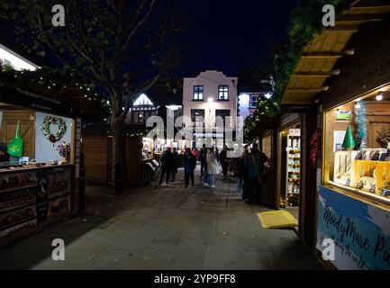 Menschen gehen durch eine festliche Weihnachtsmarktstraße, gesäumt von Holzständen, die verschiedene Weihnachtsdekorationen und Geschenke zeigen York UK Stockfoto