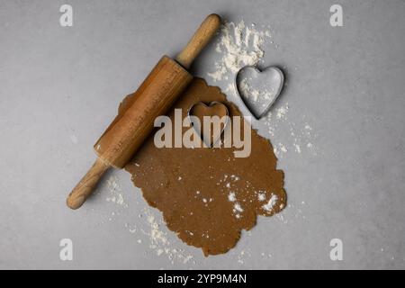 Zubereitung herzförmiger Kekse mit Nudelnadel und Ausstecher auf einer bemehlten Oberfläche in warmer Küchenatmosphäre. Stockfoto