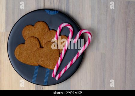 Herzförmige Lebkuchenkekse und rosa gestreifte Bonbons sind auf einem schwarzen Teller angeordnet und schaffen eine festliche und einladende Präsentation. Stockfoto