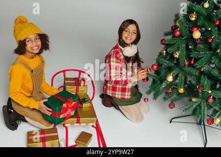 Zwei Mädchen packen fröhlich Geschenke aus und dekorieren einen Weihnachtsbaum während der Weihnachtszeit. Stockfoto