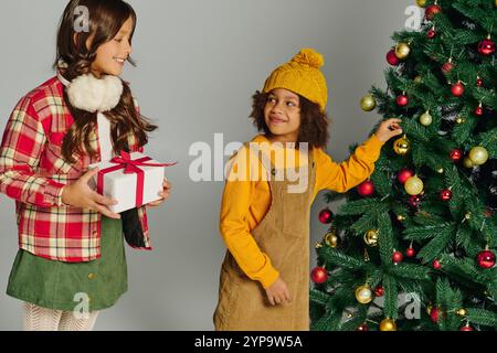 Zwei Kinder voller Aufregung, bereiten einen Weihnachtsbaum vor und teilen gemeinsam festliche Stimmung. Stockfoto