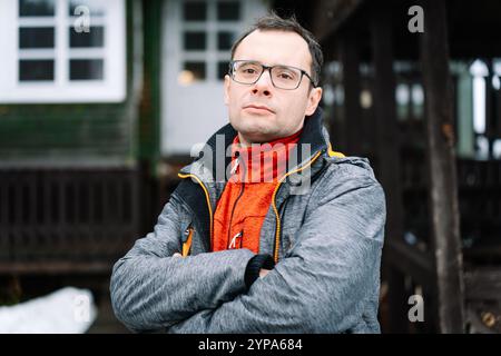 Ernster Mann in Brille und grauer Jacke bei einem Landhaus Stockfoto