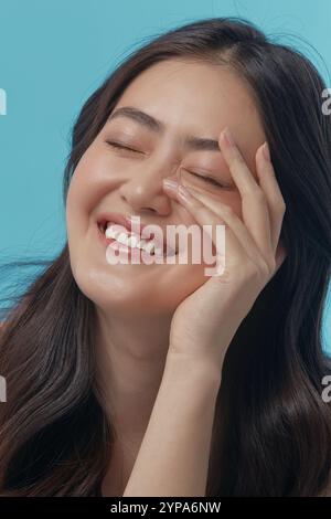 Fröhliche und verspielte junge asiatische Frau mit einer gesunden, sauberen Haut berührend auf sich selbst Gesicht und Glück Lächeln, vertikale Nahaufnahme Foto. Stockfoto