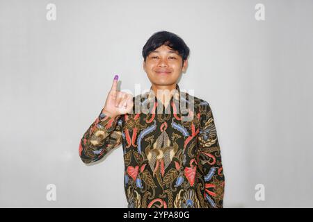 Ein Mann zeigt seinen kleinen Finger, nachdem er für die Präsidentschafts- oder Regionalwahlwahl in Indonesien gestimmt hat, indem er Batik auf weißem Hintergrund verwendet Stockfoto