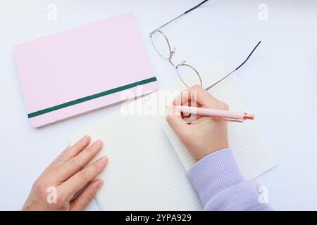 Organisierter Schreibtisch mit Notizbüchern, Stift und Brille in zartem Rosa Stockfoto