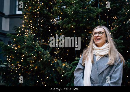 Junge Frau in Brille vor dem Weihnachtsbaum mit Lichtern Stockfoto