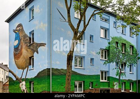 Weißgeflecktes Bluethroat (Luscinia svecica cyanecula), Wohngebäude mit einem Bluethroat und Baum als Wandgemälde nach energieeffizienter Sanierung Stockfoto