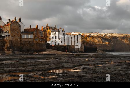 Ein kurzer Zauber der Wintersonne erleuchtet die reichen Farben der Steinhäuser und des Bay Hotels in Robin Hoods Bay, Yorkshire Stockfoto