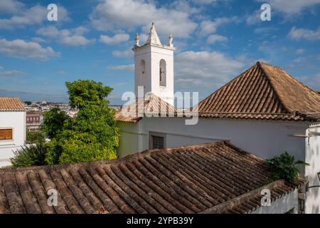 Gekachelte Dächer und Kirchturm von Igreja da Misericórdia unter blauem Himmel und Sonnenschein in der beliebten Wintersonnenstadt Tavira, Algarve, Portugal Stockfoto