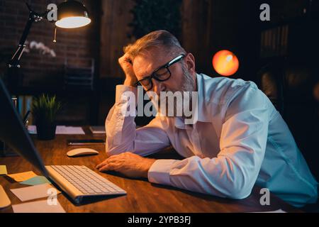 Foto von nettem alten Mann müde Schlafbekleidung weißes Hemd formalwear Coworking Abendlicht schönes Licht Büro Stockfoto