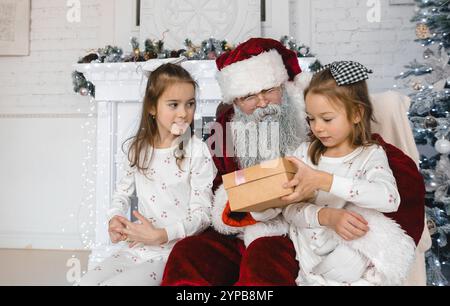 Der Weihnachtsmann teilt die Weihnachtsfreude mit zwei entzückten Mädchen im passenden Pyjama. Sie empfangen aufgeregt Geschenke in einem wunderschön eingerichteten Haus, kreieren Stockfoto