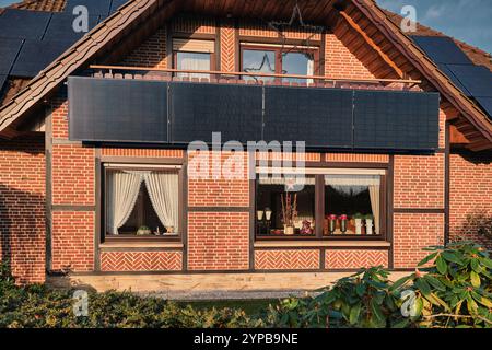 Ein traditionelles deutsches Fachwerkhaus mit vertikalen Solarpaneelen auf dem Balkon und einer charmanten Ziegelstein- und Holzfassade, die Alt und Neu verbindet. Stockfoto