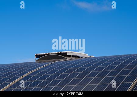 Reihen von Photovoltaik-Zellen produzieren saubere Energie auf einem modernen geschwungenen Dach Stockfoto