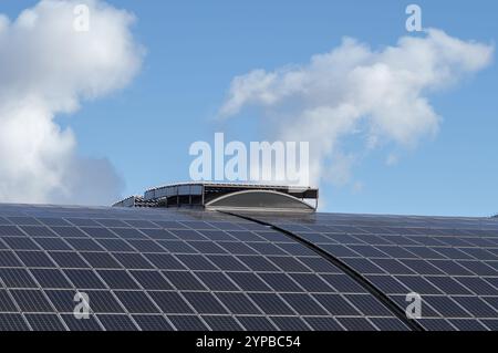 Sonnenkollektorsystem auf einem gekrümmten Dach, das Sonnenlicht unter einem bewölkten blauen Himmel einfängt und eine nachhaltige Energieerzeugung fördert Stockfoto