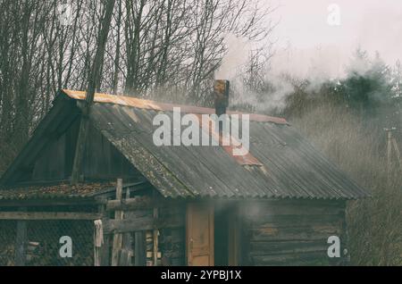 Die russische Holzsauna (ohne Marken) wird an einem Novembertag in Schwarz mit Rauch beheizt Stockfoto