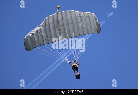 Ein Fallschirmaufklärer der Schweizer Armee an einem Freifallschirm. Im Hintergrund ein Jet mit Kondensstreifen. Die Flugshow ZigAirMeet mit internationaler Beteiligung aus dem militärischen und zivilen Luftfahrtbereich fand am 18. Und 19. August 2023 in Mollis, Kanton Glarus, Schweiz, statt. Mollis Glarus Schweiz *** Ein Fallschirmaufklärungsflugzeug der Schweizer Armee auf einem Freifallfallfallschirm im Hintergrund ein Jet mit Kondensstreifen die ZigAirMeet Luftschau mit internationaler Beteiligung aus dem Militär- und Zivilluftfahrtsektor fand am 18. Und 19. August 2023 in Mollis, Kanton Glarus, Switze statt Stockfoto