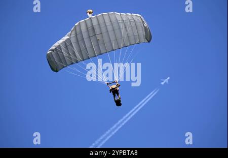 Ein Fallschirmaufklärer der Schweizer Armee am Fallschirm. Im Hintergrund ein Jet am Himmel mit Kondensstreifen. Die Flugshow ZigAirMeet mit internationaler Beteiligung aus dem militärischen und zivilen Luftfahrtbereich fand am 18. Und 19. August 2023 in Mollis, Kanton Glarus, Schweiz, statt. Mollis Glarus Schweiz *** Fallschirmjäger der Schweizer Armee auf einem Fallschirm im Hintergrund, ein Jet am Himmel mit Kondensstreifen die Luftschau ZigAirMeet mit internationaler Beteiligung aus der Militär- und Zivilluftfahrt fand am 18. Und 19. August 2023 in Mollis, Kanton Glarus, Schweiz Mollis Glarus statt Stockfoto