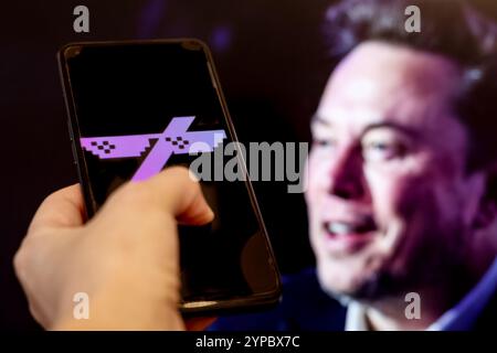 In dieser Fotoabbildung ist das Grok-Münzlogo auf einem Smartphone vor einem Computerbildschirm zu sehen, der ein Porträt von Elon Musk zeigt. Elon Musk, der Finanzberater des US-Präsidenten und der reichste Mann der Welt ist, unterstützt das Grok-Projekt öffentlich. Stockfoto