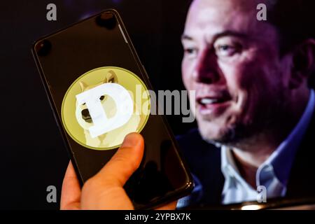 In dieser Abbildung ist das Dogecoin-Logo auf einem Smartphone vor einem Computerbildschirm zu sehen, der ein Porträt von Elon Musk zeigt. Elon Musk, der Finanzberater des US-Präsidenten und der reichste Mann der Welt ist, unterstützt das Doge-Projekt. Stockfoto