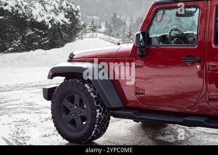 Nahaufnahme eines roten Jeeps am Wintertag. Vorderrad eines Trucks 4x4-Abenteuer im Freien. Geländewagen in dickem Wintereis und Frostschnee. Niemand Stockfoto