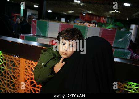 Teheran, Iran. November 2024. Eine iranische verschleierte Frau, die ihr Kind hält, nimmt an der Beerdigungszeremonie von Brigadegeneral Kiyomarth Porhashmi Teil, einem hochrangigen Offizier der Quds Force der Islamischen Revolutionsgarde (IRGC), der in Aleppo, Syrien, getötet wurde. Die Quds Force der IRGC ist eine Einheit der iranischen Revolutionsgarde, die Militär-, Geheimdienst- und Unterstützungsoperationen im Ausland durchführt, um den regionalen Einfluss des Iran voranzutreiben. (Kreditbild: © Rouzbeh Fouladi/ZUMA Press Wire) NUR REDAKTIONELLE VERWENDUNG! Nicht für kommerzielle ZWECKE! Stockfoto