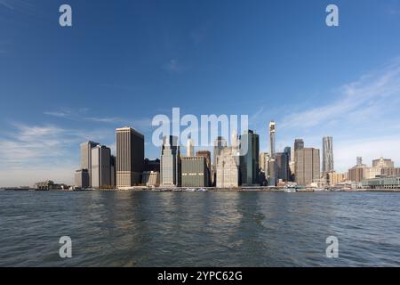 Eine pulsierende Skyline der Stadt erhebt sich vor einem klaren blauen Himmel, der sich im ruhigen Wasser unter ihnen spiegelt und moderne Architektur und urbanes Leben verkörpert. Stockfoto