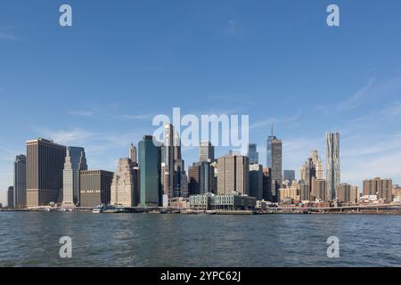 Eine atemberaubende Skyline der Stadt erhebt sich unter einem klaren blauen Himmel, deren moderne Architektur sich wunderschön im ruhigen Wasser darunter spiegelt Stockfoto